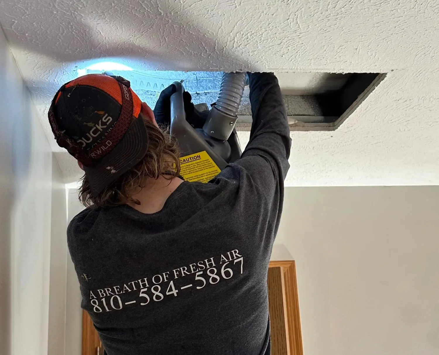 Air duct cleaning technician working a ceiling duct in Flushing